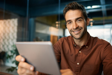 Obraz premium Smiling businessman working on a digital tablet in an office