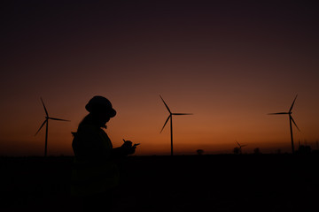 Silhouette of women engineer working and holding the report at wind turbine farm Power Generator Station on mountain,Thailand people