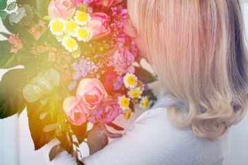 Blonde hair girl with pink spring flowers bouquet at white wall. Woman hiding head bouquet pink flowers. 