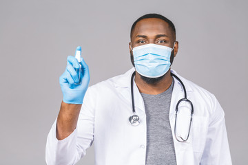 African american doctor man in gown face mask gloves isolated on grey background. Epidemic pandemic coronavirus 2019-ncov sars covid-19 flu virus. Holding bottle liquid antibacterial sanitizer.