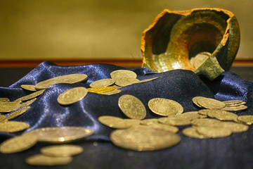 Antique gold coins scattered on silk next to a broken pot