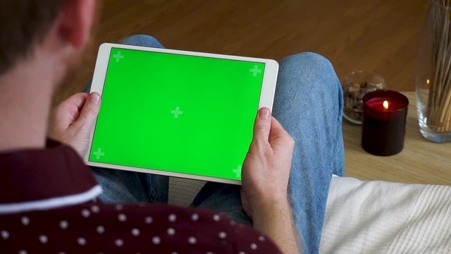 Male hands holding tablet with a green screen horizontally and watching a video
