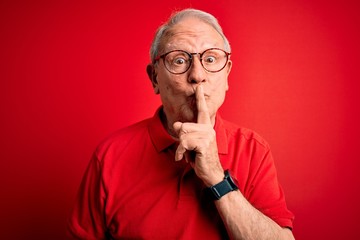 Grey haired senior man wearing glasses and casual t-shirt over red background asking to be quiet with finger on lips. Silence and secret concept.