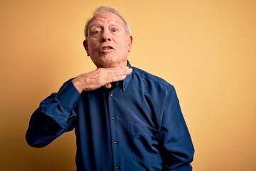 Grey haired senior man wearing casual blue shirt standing over yellow background cutting throat with hand as knife, threaten aggression with furious violence