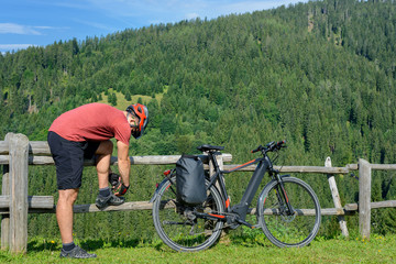 Man cyclist tying shoelace near to bicycle on the mountain