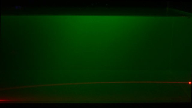 A red laser beam shines trough a green flourescent liquid. The beam is deflected due to an irregular distribution of sugar in the liquid.
