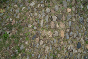 Antique paving stones. Stone and grass floor. Natural stone wall texture. Medieval masonry. Ancient wall. Stone brick wall. Macro texture. Medieval architecture. Rough masonry. Background texture.