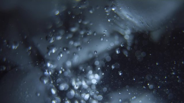 Pieces of ice float in the liquid. Bubbles rise and envelop ice. Very beautiful macro bokeh.