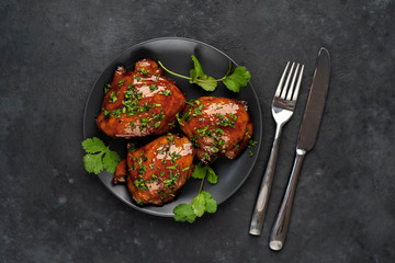 Grilled sweet chicken thighs with herbs and spices on a black plate on a stone background
