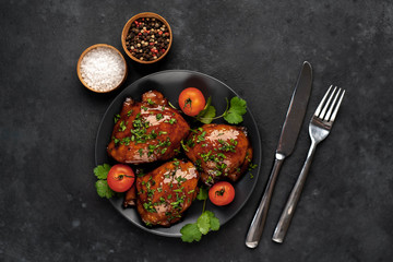 Grilled sweet chicken thighs with herbs and spices on a black plate on a stone background