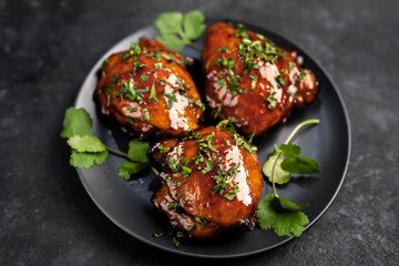 Grilled sweet chicken thighs with herbs and spices on a black plate on a stone background