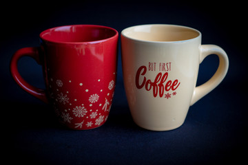 Two red and beige coffee cups with lettering on dark black background