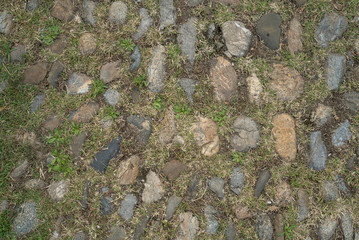 Antique paving stones. Stone and grass floor. Natural stone wall texture. Medieval masonry. Ancient wall. Stone brick wall. Macro texture. Medieval architecture. Rough masonry. Background texture.
