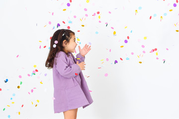 Portrait of a beautiful little girl wearing dress standing under confetti rain and celebrating over white background.