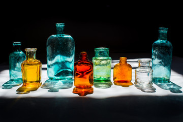 Colorful small glass bottles in sunlight on black background. Reflected light in the sun. Background glass. 