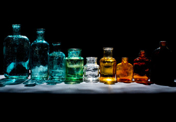 Colorful small glass bottles in sunlight on black background. Reflected light in the sun. Background glass. 