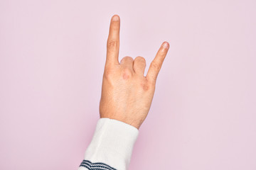 Hand of caucasian young man showing fingers over isolated pink background gesturing rock and roll symbol, showing obscene horns gesture