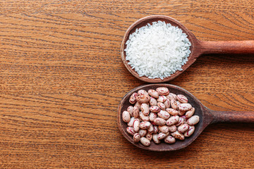 White rice and pinto beans on wooden kitchen spoons. Brown, wooden background.