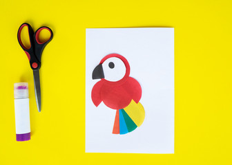 Step by step children's cardboard crafts - colored parrot on a white paper sheet. Scissors, glue,...