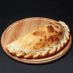 tasty calzone on a wooden tray on a black background