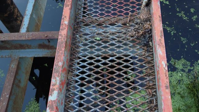 walking on an old rusty mesh metal bridge over water