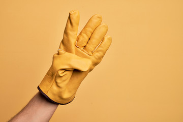 Hand of caucasian young man with gardener glove over isolated yellow background counting number 4...