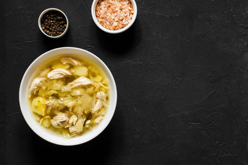Vegetable chicken soup with cabbage and potatoes in a white plate on a black table. Fresh healthy hot homemade broth. Light lunch. Top view, copy space
