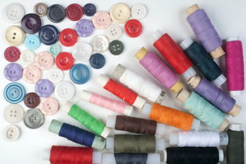 Multicolored buttons and threads are spread on white background