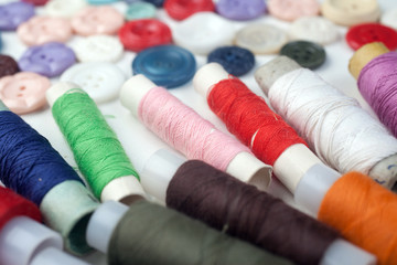 Multicolored buttons and threads are spread on white background