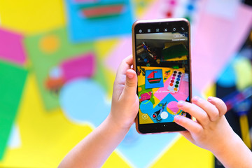 child takes a photo of his craft on a smartphone in order to send homework to the teacher. distance...