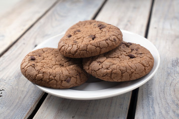 Oatmeal cookies with chocolate crumb on a white iarel on a bright wooden background