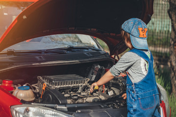 Little child trying to fix broken real car. Dreaming to be auto technician