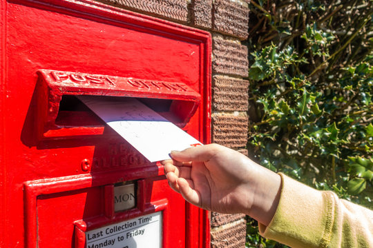 A child's hand posting a letter into a post box embedded into a brick pillar.