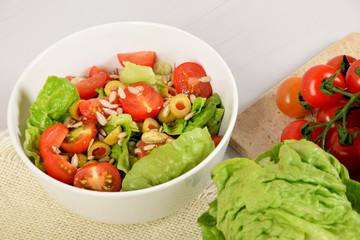 green lettuce with tomatoes, green olives and sunflower seeds in a white bowl