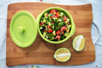 Chopped cucumber tomato salad in a green bowl. Lemon cut in half . fresh vegetable salad with tomato, cucumber and green onion on Cutting board.