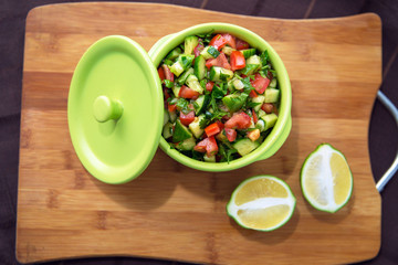 Chopped cucumber tomato salad in a green bowl. Lemon cut in half . fresh vegetable salad with tomato, cucumber and green onion on Cutting board.