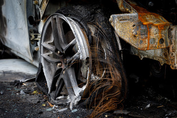 Wheel of burned car. Burnt flat tire on the car is on the gray asphalt road.