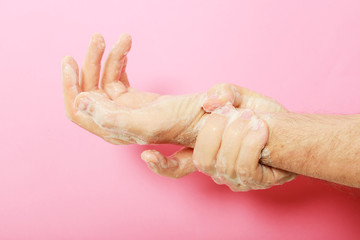 Fototapeta premium manos de hombre lavándose con jabón sobre fondo rosa.