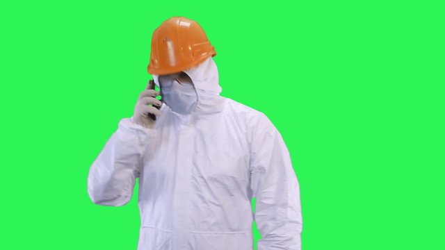 A man in a helmet and a protective suit is talking on the phone in high tones.Green screen background.