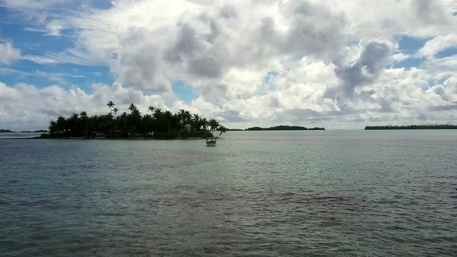 Panning across the spectaular blue lagoon and coral reef break with palm tree filled islands and a small fishing boat of this aerial drone shot in Rangiroa, French Polynesia