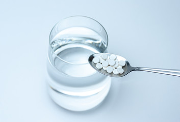 tablet in a spoon on a background of a glass of water