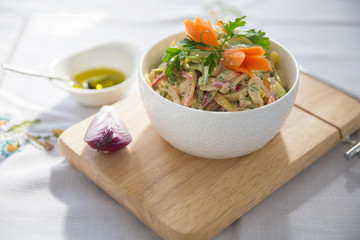 Chopped red onion . olives on a small white bowl . wooden board . Salad with ham, red and orange pepper, mushrooms, pickles, white sauce, on a white bowl and olives.