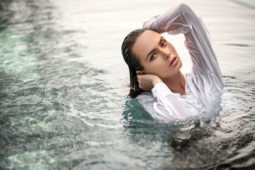 Portrait of an Attractive young woman in wet white shirt resting  in a pool.