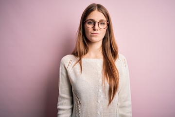 Fototapeta premium Young beautiful redhead woman wearing casual sweater and glasses over pink background looking sleepy and tired, exhausted for fatigue and hangover, lazy eyes in the morning.