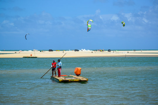 Genipabu village, Extremoz, near Natal, Rio Grande do Norte, Brazil on February 8, 2014. Two men crossing the Ceara-mirim river in a small boat and kite surfers in the background