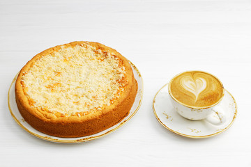 Closeup homemade cheesecake with streusel and cup of coffee cappuccino on white wooden table