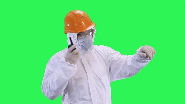 A man in a helmet and a protective suit speaks on the radio and gives out commands.Green screen background.