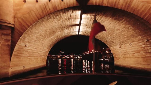 Shimmering French flag attached to the stern of a motor boat against the backdrop of the Elfel Tower at night. the ship swims under the bridge