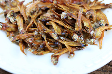 Fried giant catfish and pile of Deep fried small fishes (Minnow fish) Traditional Thai recipes in white dish on rustic wood background.  popular in Thailand, important export product of Thailand.
