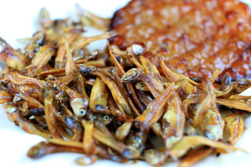 Fried giant catfish and pile of Deep fried small fishes (Minnow fish) Traditional Thai recipes in white dish on rustic wood background.  popular in Thailand, important export product of Thailand.